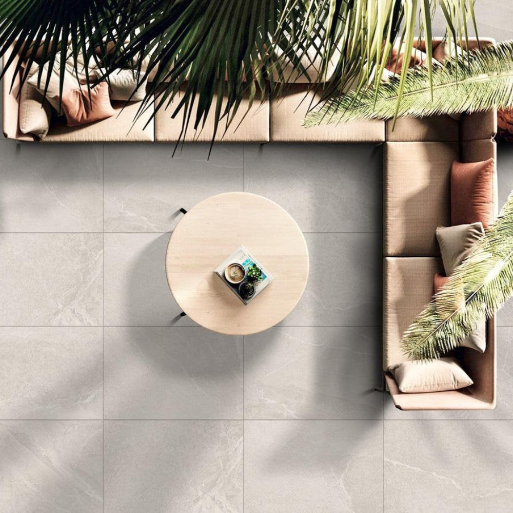 Bodo White tiles in a modern outdoor seating area with a round wooden table and pink sofa against a white coloured tiled floor