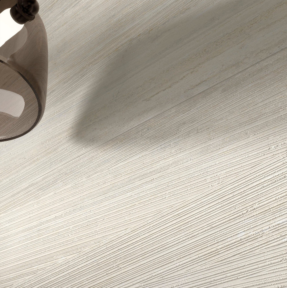 Close-up of a textured MGM Ceramiche Travertino Bianco Vein Cut floor with a lamp casting a shadow.