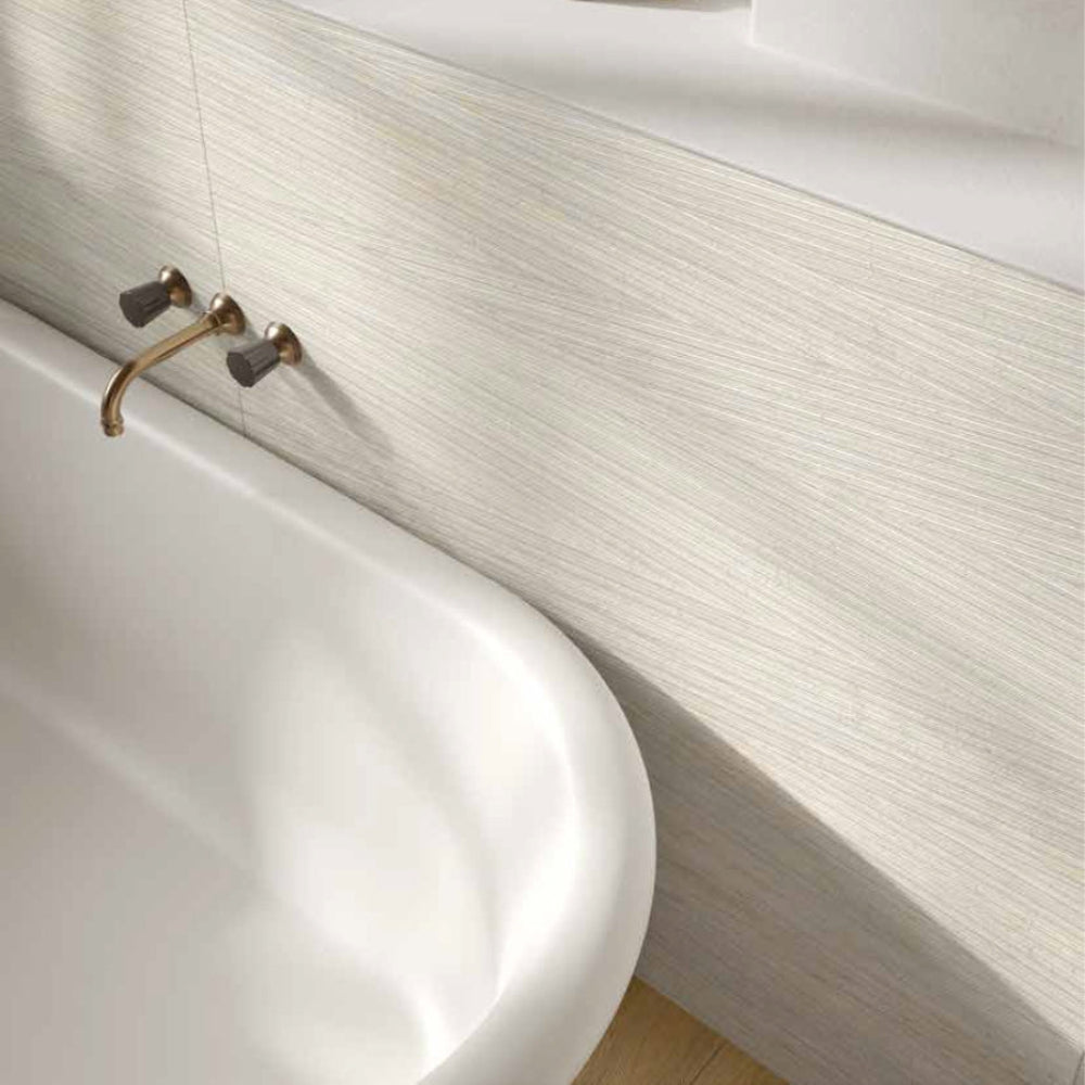 Bathroom with a white bathtub, tiled MGM Ceramiche Bianco travertino wall, and window.