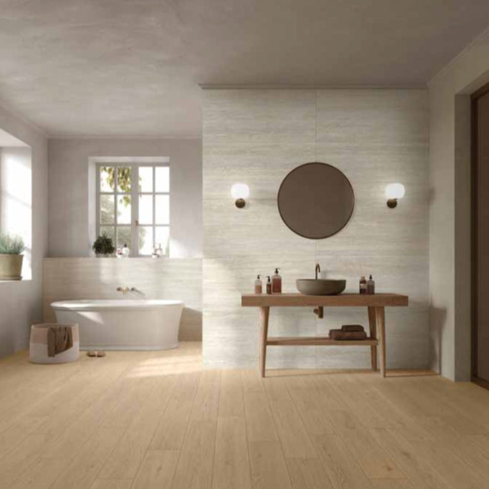 Modern bathroom with a MGM Ceramiche Travertino Bianco Vein Cut tiles wall feature and bathtub, wooden vanity, and round mirror.
