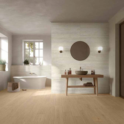Modern bathroom with a MGM Ceramiche Travertino Bianco Vein Cut tiles wall feature and bathtub, wooden vanity, and round mirror.